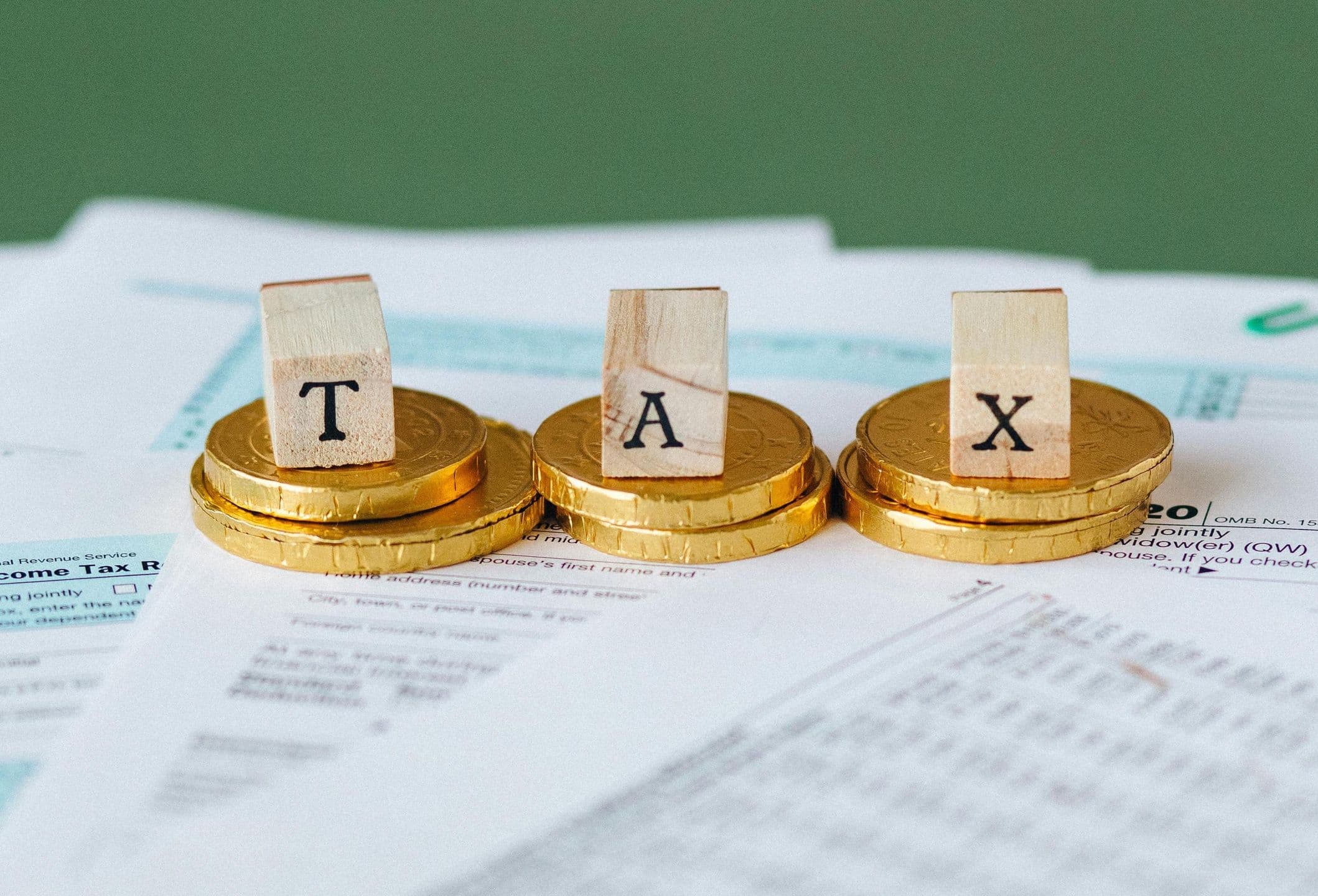Wooden blocks spelling 'TAX' placed on stacked gold coins, atop scattered tax documents, symbolizing financial and taxation concepts.